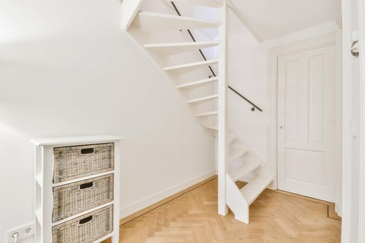 White hallway with wooden stairway leading to second floor of modern luxury apartment with minimalist interior design