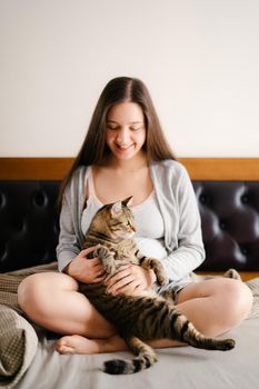Pregnant woman sitting on bed with cat. High quality photo