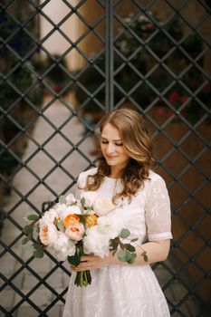 Bride in a white dress with a bouquet of flowers stands near the decorative gate. High quality photo