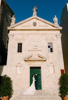 Bride and groom stand on the steps of the Catholic church of Saint apostle Mark. Perast. Montenegro. High quality photo