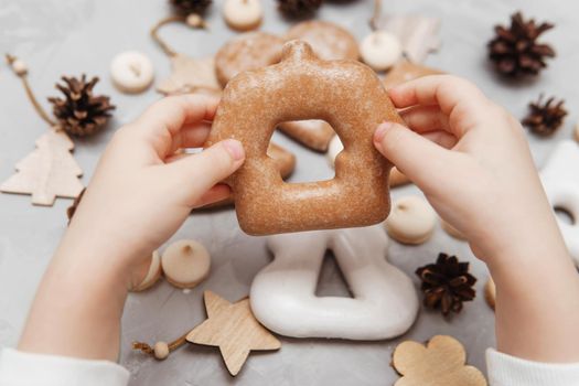 Children's hands hold a gingerbread in the shape of a home. The concept of Christmas sweets, toys, garlands and bokeh. Decor for New Year holidays.