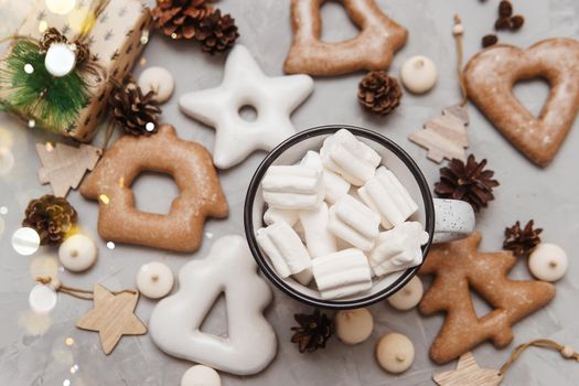 A cup of cocoa with marshmallows and New Year's gingerbread and a gift on the table, bokeh lights in the foreground. The concept of desserts and drinks during the Christmas holidays.