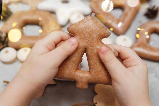 Children's hands hold a gingerbread in the shape of a Christmas tree. The concept of Christmas sweets, toys, garlands and bokeh. Decor for New Year holidays.