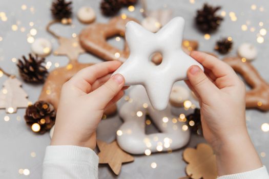Children's hands hold a gingerbread in the shape of a star. The concept of Christmas sweets, toys, garlands and bokeh. Decor for New Year holidays.