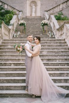 Bride is embracing groom on the stone steps near the old villa. High quality photo