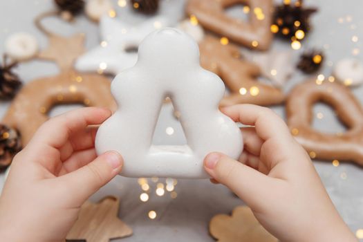 Children's hands hold a gingerbread in the shape of a Christmas tree. The concept of Christmas sweets, toys, garlands and bokeh. Decor for New Year holidays.