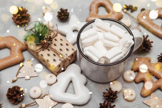 A cup of cocoa with marshmallows and New Year's gingerbread and a gift on the table, bokeh lights in the foreground. The concept of desserts and drinks during the Christmas holidays.