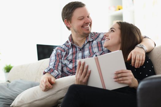 Portrait of middle aged father and young daughter reading book together sitting on couch at home. Happy emotion and quality time together. Family concept