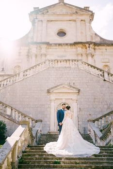 Bride and groom stand on the stone steps near the ancient church. High quality photo