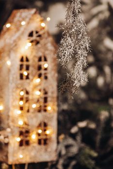 Piece of a tree branch in snow hanging down in front of a dollhouse, decorated with string lights. New year concept