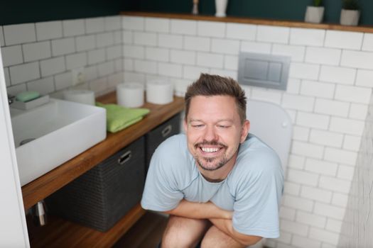 Portrait of man feeling relief after using toilet, fulfill natural need. Man in room with modern interior, white tiles, trendy decor. Nature calls concept