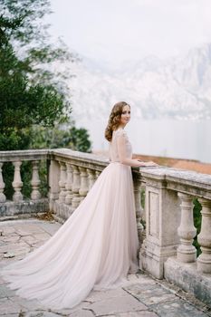 Bride stands on a stone terrace leaning on a balustrade. High quality photo