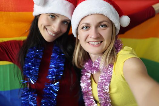 Portrait of female lovers happy about new year celebration hold lgbt flag. Smiling couple posing for picture. New year party, christmas, holiday concept