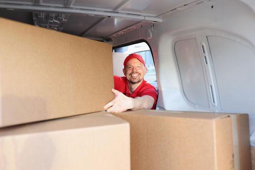 Portrait of cheerful man on work put boxes in truck for further delivery on address. Happy man help with relocation and load belongings. Helper concept