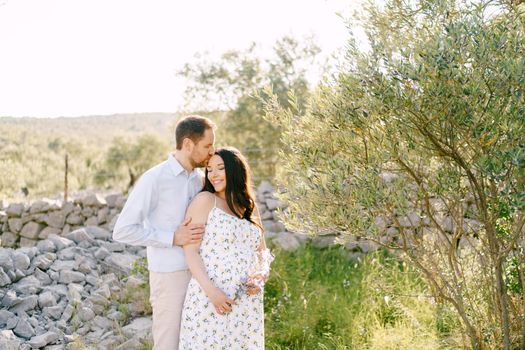 Man kissing the head of a pregnant woman holding wildflowers. High quality photo