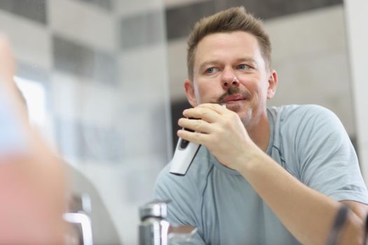 Portrait of middle aged man shaving beard with electronic machine. Device for quick face care, get ready in morning. Good morning, beauty treatment concept