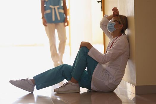 Low angle of exhausted surgeon after long operation sitting in hospital corridor. Bad news, rest after hard operation. Medicine, save life, health concept