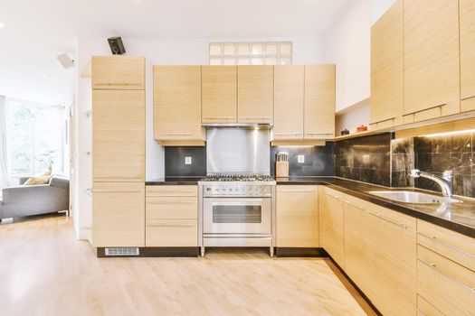 Interior of contemporary open plan kitchen with built in appliances and cabinets under ceiling with wooden beams in light
