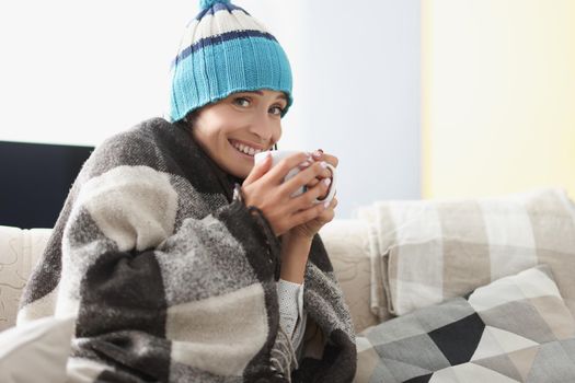 Portrait of sick woman having cup of hot tea drink covered with warm blanket. Unwell girl rest at home on self isolation. Covid, health, quarantine concept