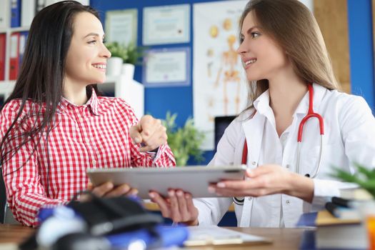 Portrait of patient and family doctor talking about health checkup, sign prescription on tablet. Smiling client and doctor in clinic. Appointment concept