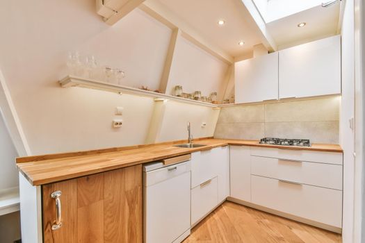 Interior of contemporary open plan kitchen with built in appliances and cabinets under ceiling with wooden beams in light