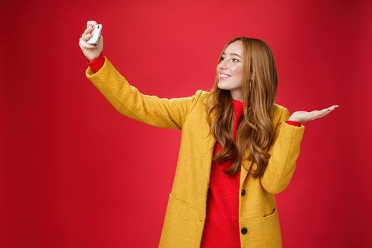 Cute redhead woman walking in park deciding take selfie near beatiful scenery or cute animal extending hand with smartphone smiling broadly at device as taking photo and pointing at something. Technology and lifestyle concept