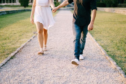 Man and woman walking along the gravel path in the park holding hands. High quality photo