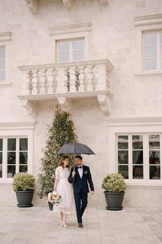 Bride and groom with an umbrella walk through the courtyard of an old villa. High quality photo
