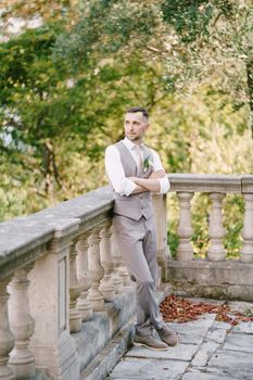 Groom folded his arms over his chest and leaned against the stone fence in the garden. High quality photo