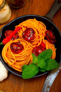 italian spaghetti pasta and tomato with mint leaves on iron skillet over wood board 