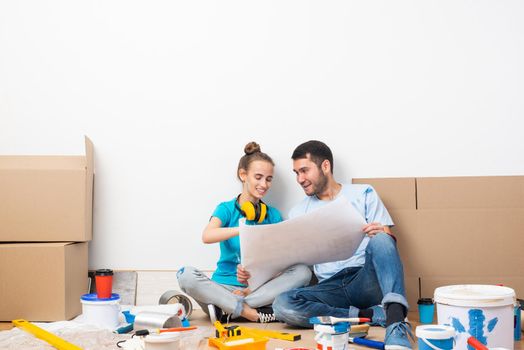 Couple discussing home redesign ideas. Man and woman together planning new home interior design. Cardboard boxes, painting tools and materials on floor. House remodeling and architectural renovation.