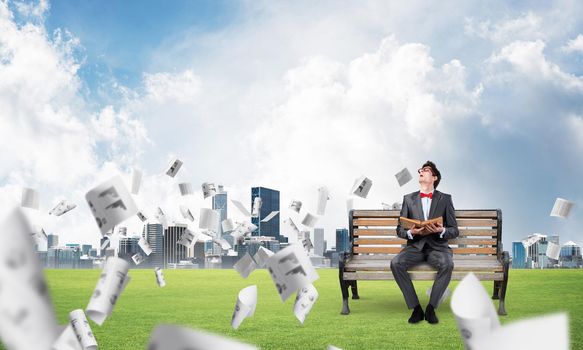 young student with a book on the bench, flying around in the chaos of paper