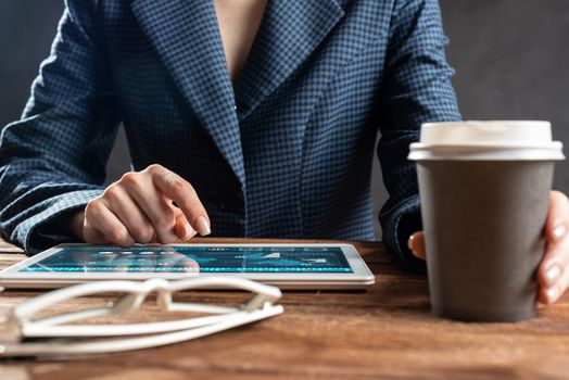 Businesswoman using tablet computer at wooden desk. Close up woman hand pointing on touchscreen. Business application with online financial analytics on screen of tablet device. Strategy planning