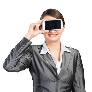 Portrait of happy woman covering her eyes with smartphone. Businesswoman showing mobile phone with blank screen. Corporate businessperson isolated on white background. Mobile communication layout