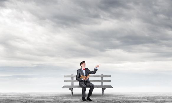 Student sits on a bench, holding a book. Traditional education concept