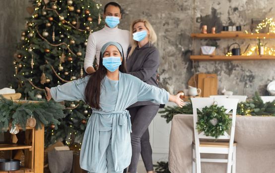 A happy family wear medical masks due to the COVID-19 coronavirus near Christmas tree. Xmas holidays.