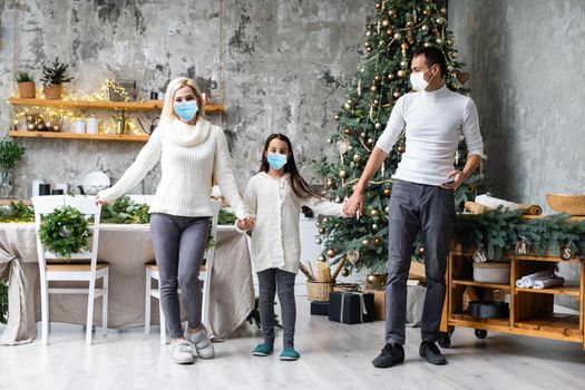 A happy family wear medical masks due to the COVID-19 coronavirus near Christmas tree. Xmas holidays.