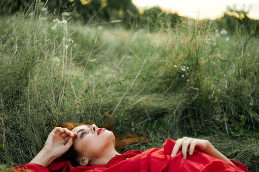 pretty woman in red dress lies on the grass freedom landscape. High quality photo