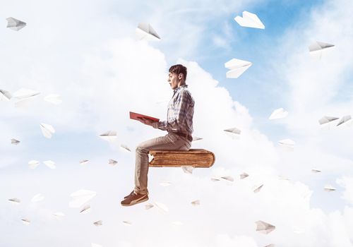 Young man in casual sitting on old book with one in hands