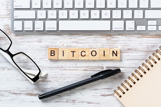 Bitcoin cryptocurrency concept with letters on cubes. Blockchain and digital money. Still life of workplace with supplies. Flat lay vintage wooden desk with computer keyboard and spiral notebook.