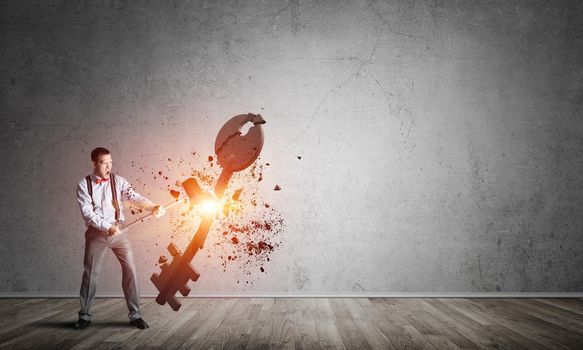 Determined businessman in empty interior breaking with hammer stone key figure