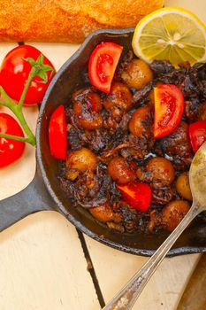 Baby cuttle fish roasted on iron skillet with tomatoes and onions over rustic wood table