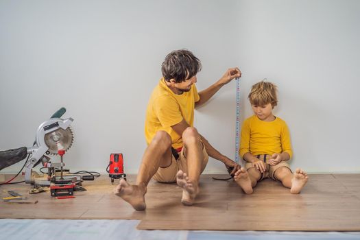 Father and son installing new wooden laminate flooring on a warm film floor. Infrared floor heating system under laminate floor.