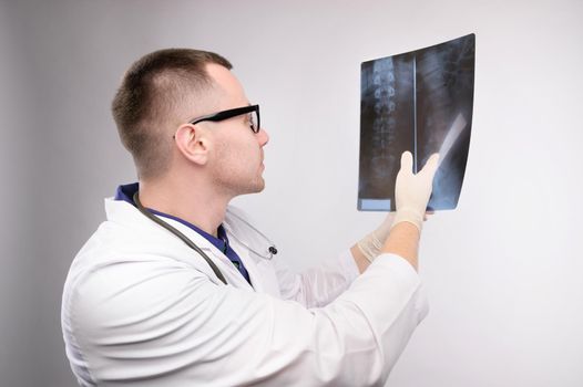 Young caucasian doctor a radiologist is looking at an x-ray. A doctor in a white coat with glasses with a stethoscope holds an x-ray in his hand.