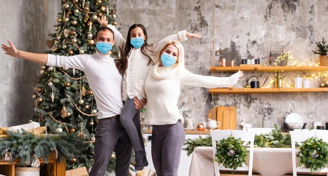 A happy family wear medical masks due to the COVID-19 coronavirus near Christmas tree. Xmas holidays.