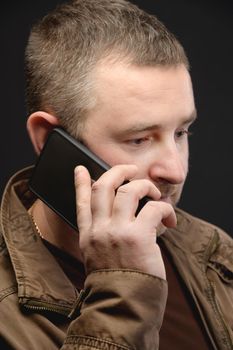 An anxious middle-aged man calls and talks on the phone. Close-up. Studio portrait.