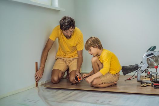 Father and son installing new wooden laminate flooring on a warm film floor. Infrared floor heating system under laminate floor.