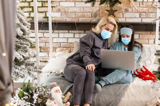 Mom and daughter in medical masks on their face call up with relatives on a computer to wish merry christmas.