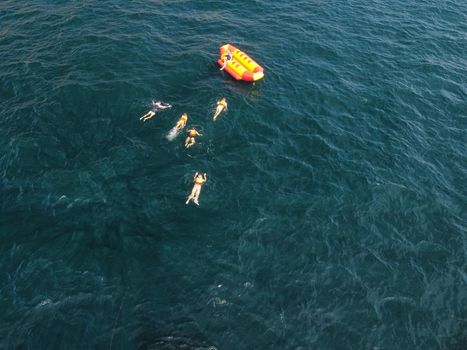 Happy people swim on air mattress behind a high speed water bike. Tourists ride on inflatable watercraft boat. Sea attraction. Water boat skating people on large Inflatable raft. Aerial copter view