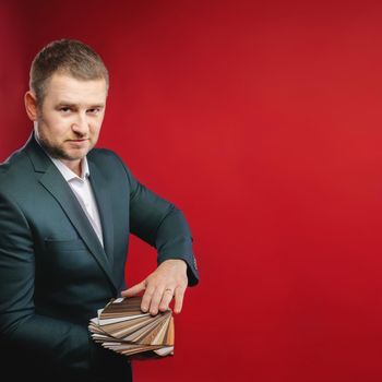 Confident business leader or manager standing in the studio with samples of furniture coverings, smiling at the camera. Caucasian businessman owner of his own furniture business.